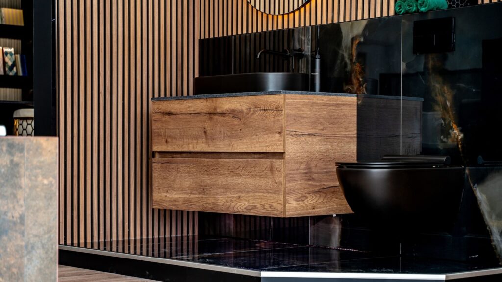 A modern, dark wood floating vanity with a black sink and faucet. The bathroom features vertical wood paneling and black marble-style tile.